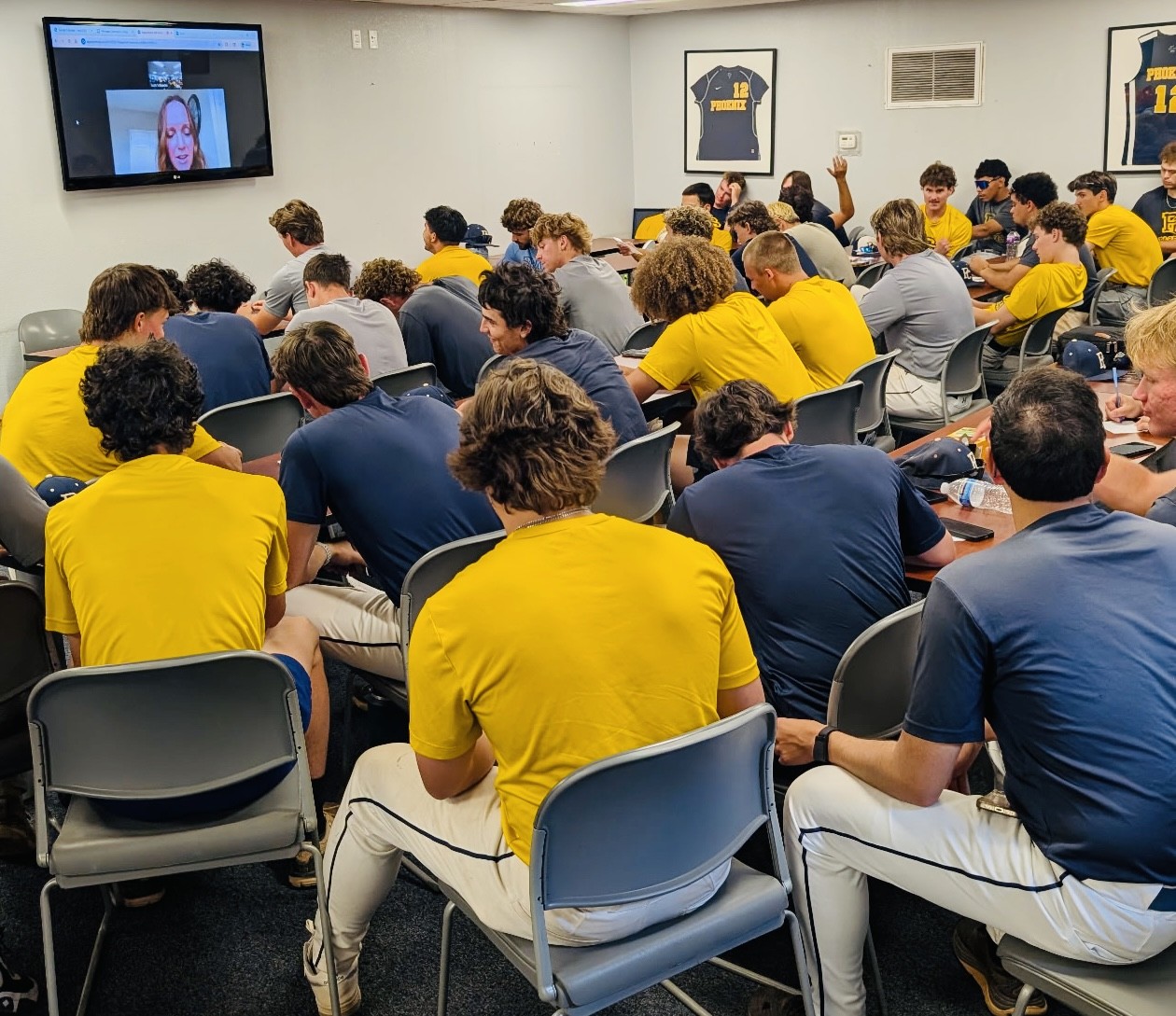 team in classrooms watches instructor on video screen