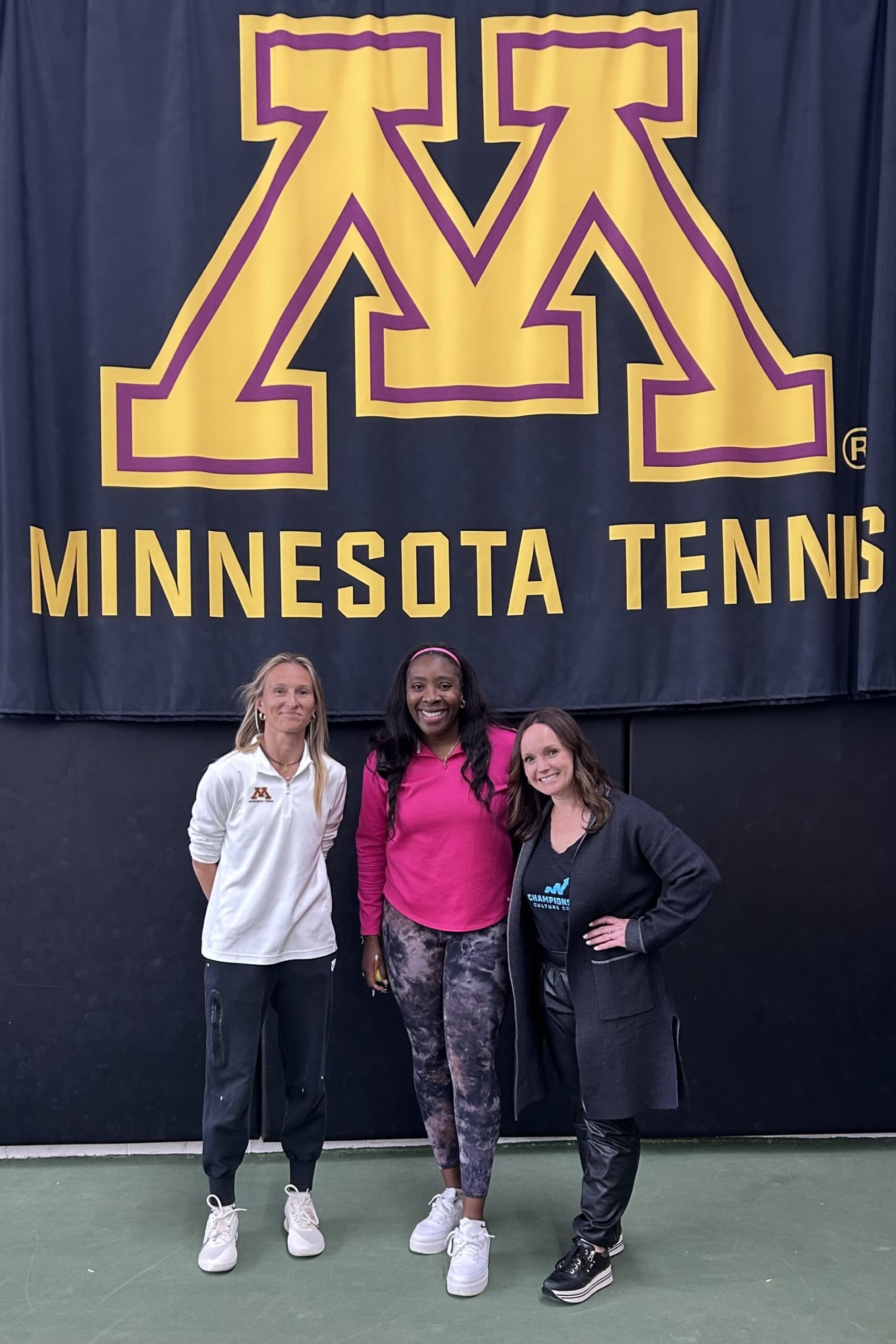 three women in front of "Minnesota Tennis" sign