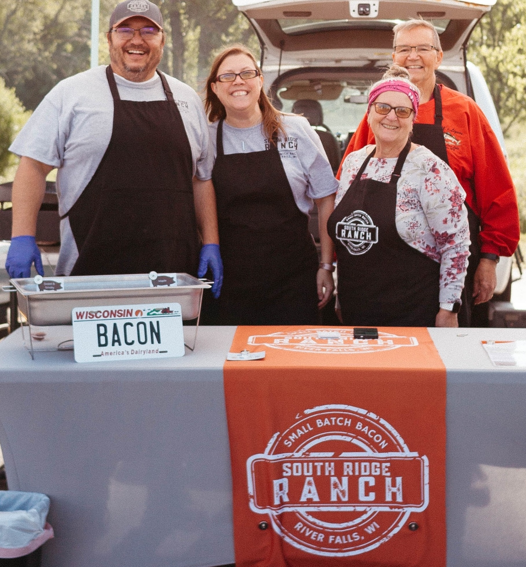 four adults at farmers market standing at South Ridge Ranch Bacon table