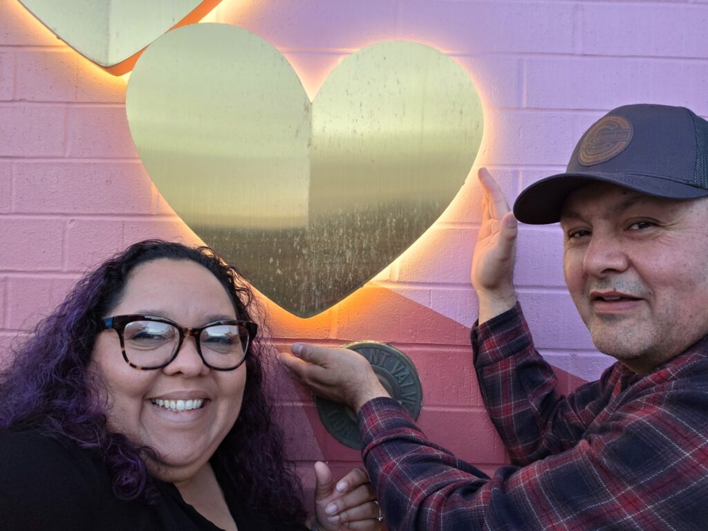 Mykeerah and husband posing in from of a heart display on a wall